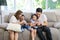 Asian family having fun in singing karaoke on sofa in living room together. Mother teaching son child and looking he singing song