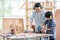 Asian father with noise canceling headphone teach and show to his son to use electric drill to work with woodwork in their house.