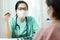 Asian female Doctor in green uniform wear glasses and surgical mask talking, consulting and giving advice to Elderly woman patient