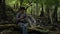 Asian female ecologist sitting on wooden log near waterfall and texting message on smartphone in tropical forest.