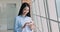 Asian female employee using smartphone standing in office hallway