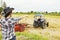 Asian female farmer working in the rice field directs the workers driving the tractor to collect the straw.