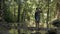 Asian female hiker with backpack takes a photo with mobile phone in tropical forest while standing among small creek during summer