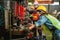 Asian female and male manufacturing workers operating steel drilling machine together in line of metal work production factory