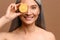 Asian female with radiant and smooth face skin covering eye with piece of lemon