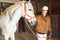 Asian female stable worker leading horse by bridle in barn