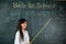 Asian female teacher smiling with wooden stick pointing to blackboard