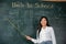 Asian female teacher smiling with wooden stick pointing to blackboard