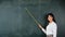 Asian female teacher smiling with wooden stick pointing to blackboard