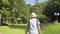 Asian female tourist wearing straw hat and backpack is walking leisurely on the grass in forest park under sunlight.