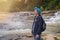 Asian female trekker with travel gear, backpack and crutches stands by the waterfall in the forest, admiring the beauty of nature