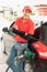 Asian gas station worker man leaning against black car with happiness while green fuel nozzle filling high energy power fuel into