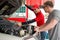An Asian gas station worker raises the car bonnet to check for the cause of an engine malfunction. A caucasian driver with