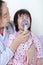 Asian girl having respiratory illness helped by health professional with inhaler.