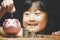 Asian girl holding a coin to put in a piggy bank in close-up and coins stack