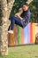 asian girl playing funny face by climbing on tree branch in public park with happiness emotion