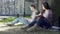 Asian girl reading book under tree and looking at guy using laptop, shyness