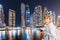 Asian girl with smartphone in her hand walking and exploring the grand Marina district in Dubai with the Bay and skyscrapers