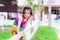 Asian girl wearing a rainbow-colored dress is climbing the white fence of playground to cross shore. Field has green grass.