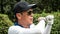 Asian golfer hitting golf in cap and sunglasses playing golf