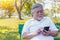 Asian grandfather chatting with family by using smart phone and internet online at park. Old man family stay at foreign country. E