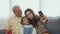 Asian grandparents laughing taking selfie with granddaughter on sofa at home by mobile