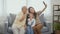 Asian grandparents laughing taking selfie with granddaughter on sofa at home by mobile