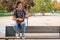 Asian guy smiling and playing acoustic Ukulele guitar sitting on a bench.