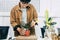 Asian haircut women in a brown jacket and grey shirt taking care of a plant house with a tree on pot hobby at home