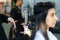 Asian hairdresser curls hair for customer with ceramic curler at beauty salon