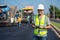 Asian handsome civil engineer under inspection and survey workplace by tablet with Asphalt paver & road roller & dump truck and