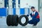 Asian handsome mechanic in uniform is sit and hold the Car tire wheel with the thumb up in car repair center