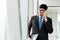 A asian handsome young businessman holding his laptop tablet while using his phone and standing on the escalator. Business concept