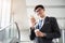 A asian handsome young businessman holding hot coffee cup while using his phone and standing on the escalator. Business concept