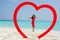 Asian happy girl in a red dress standing at the tropical beach inside heart