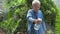 Asian happy senior grandfather caring and watering the plants with spray bottle in the backyard at home. Hobbies and leisure.