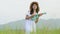 Asian happy woman in white dress playing ukulele guitar in green meadow field with mountaing background on summer. Musician beauty