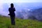 Asian hiking or tourist woman in dark blue sweater with camera standing on green grass field with mountain view and mist