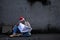Asian homeless aged man upset wearing red christmas hat sitting on roadside reading newspaper about politics and economy, Aged man