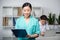 Asian internist holding clipboard with diagnosis, doctor sitting behind in professional clinic