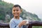 Asian kid boy is drinking water from the glass. With mountain views background