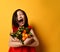 Asian kid in red blouse. Laughing out loud, holding an armful of tangerines and oranges, posing on orange background. Close up