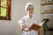 Asian lady in bathrobe with facial anti aging clay mask is reading a book in her living room