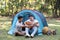 Asian LGBTQ couple enjoying nature, camping with tents in the forest area by the river, playing guitar.
