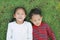 Asian little child boy and girl lying on green grass outdoors in summer park. Portrait of sister and brother resting in garden