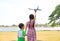 Asian little child girl hold hands baby boy and raise up a blue toy airplane flying on air in the nature garden. Sister and her