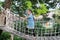 Asian little child girl playing on suspension wooden bridge. Kid walking on rope bridge Equipment at park playground