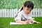 Asian Little Chinese girl kneeling on the grass and doing homework