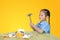 Asian little girl in school uniform breaking piggy bank isolated on yellow background at table. Schoolgirl with Money saving