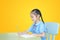 Asian little girl in school uniform writing on notebook at desk isolated over yellow background. Schoolgirl and Education concept